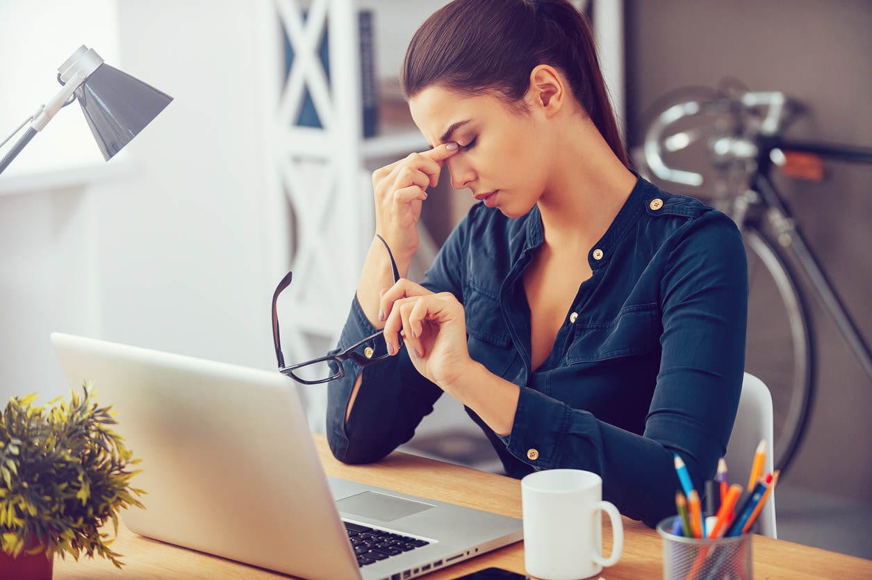 Frustrated young woman keeping eyes closed and massaging nose while sitting at her working place in office