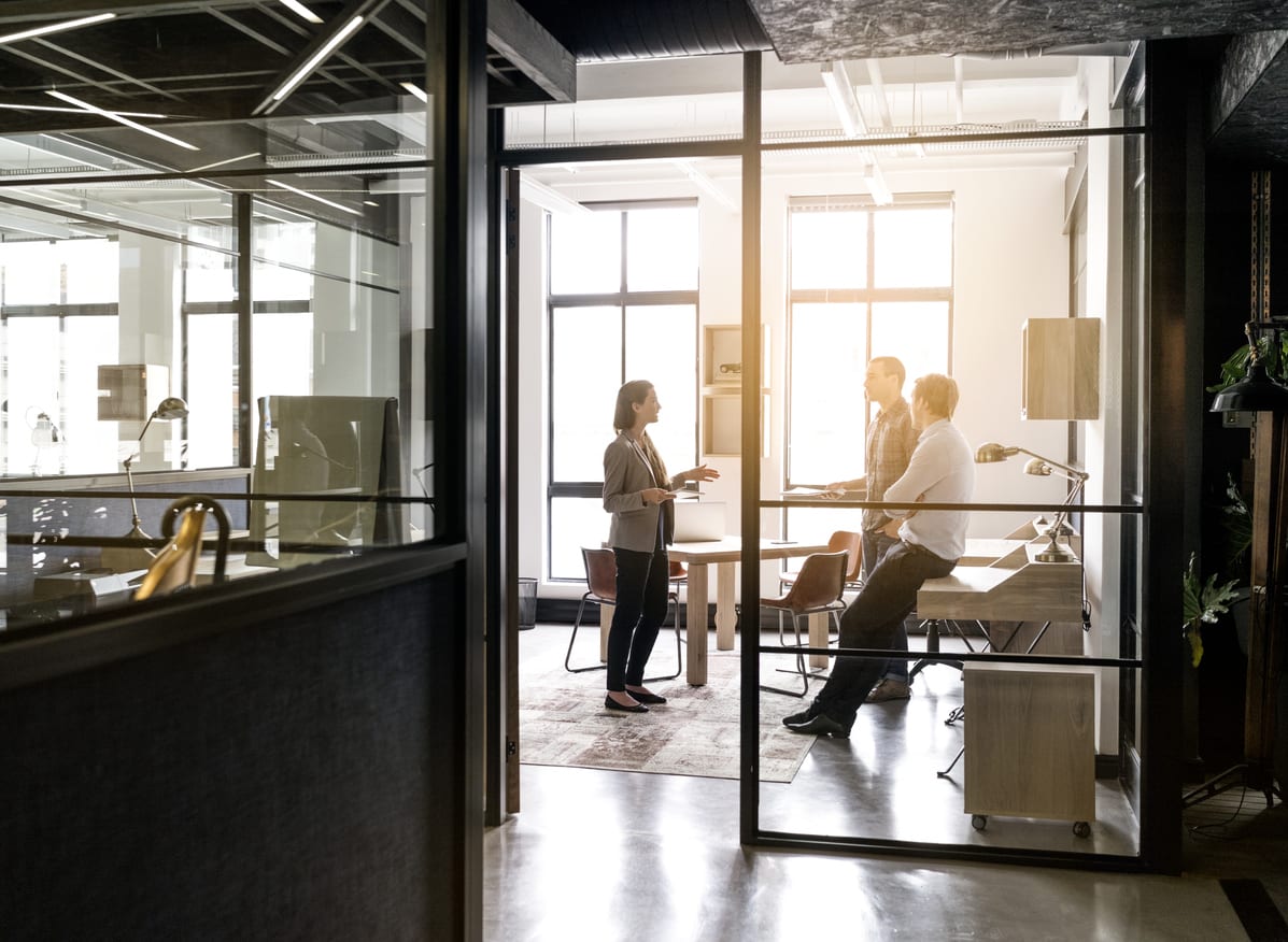 Businesswoman explaining strategy to colleagues seen through glass walls in office. Female professional is giving presentation to executives in board room. All are in meeting.