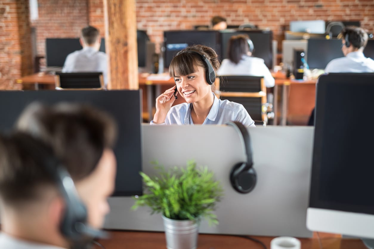 Call center worker accompanied by her team. Smiling customer support operator at work. Young employee working with a headset.