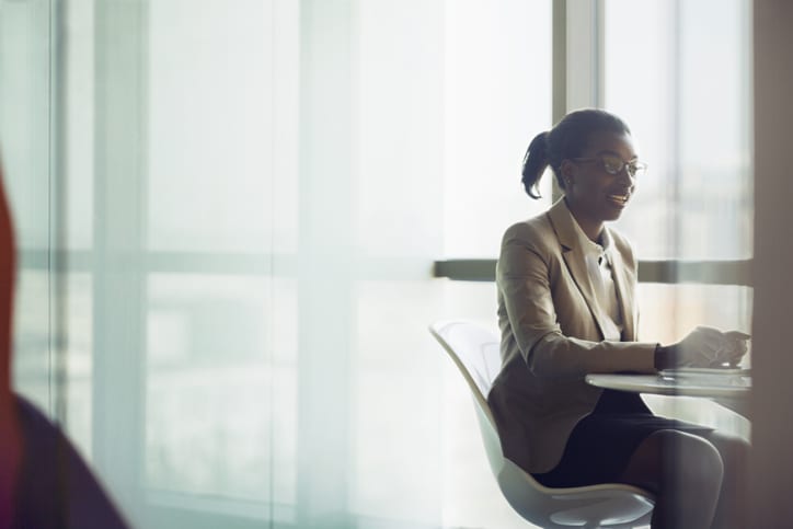 Young Black businesswoman sitting in meeting room area with anonymous client to explain discuss talk about products and services and ideas in bright sunny modern contemporary office space