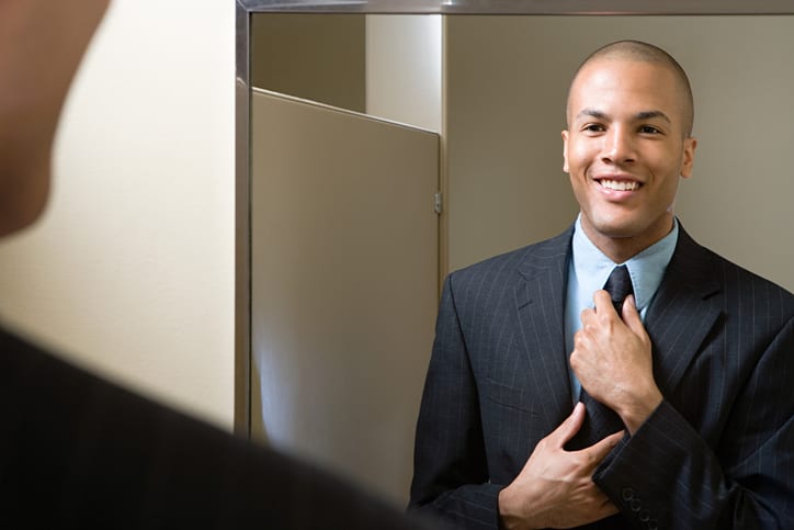 Man adjusting tie in mirror