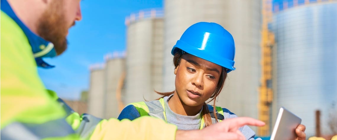 Male and female colleagues in high vis jackets and hard hats discussing a problem using a laptop