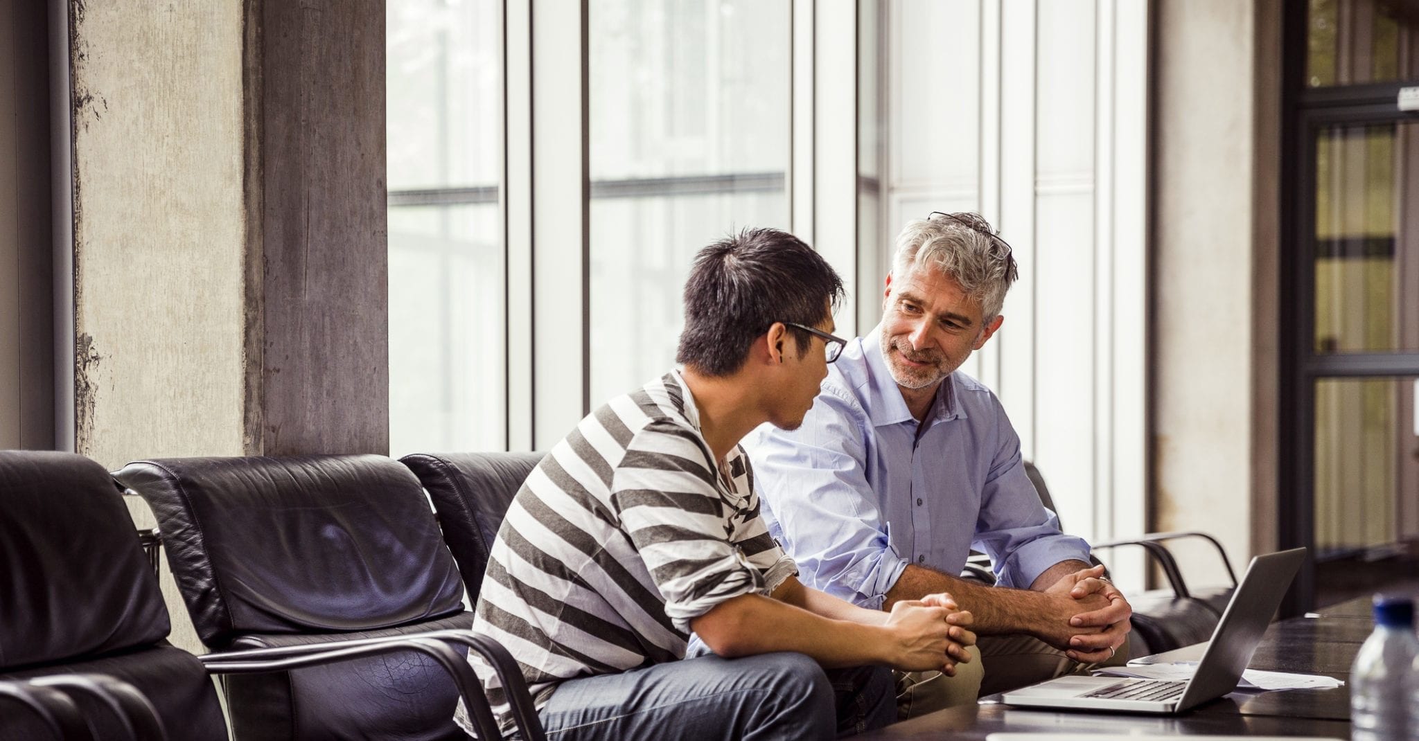 Close up of two men sitting together in deep discussion with a table and laptop in front of them