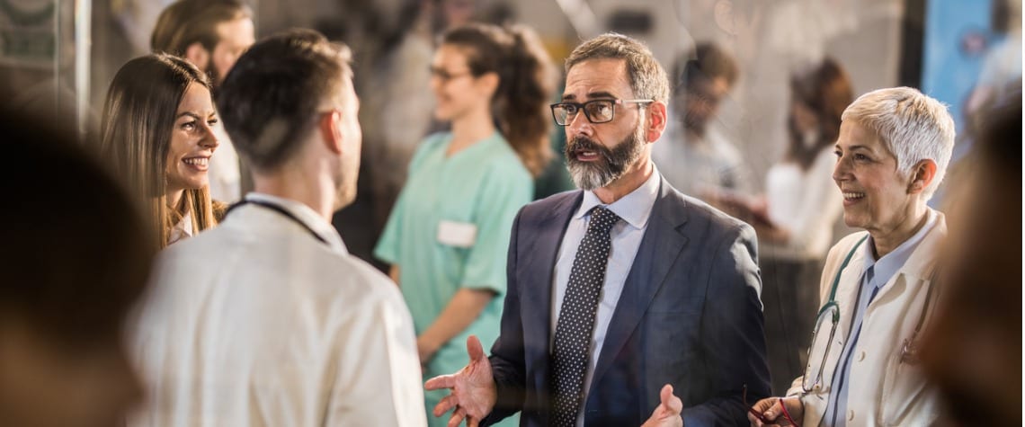 Businessman speaking with three male and female colleagues at networking event