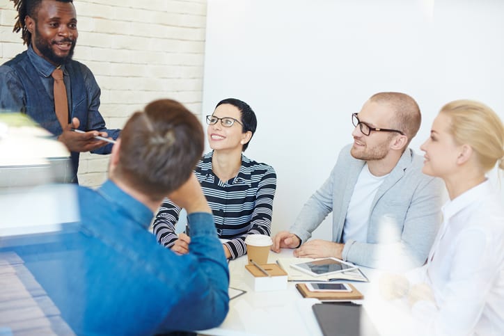 Group of executives at conference table in office listening intently to lively charismatic Afro-American colleague presenting idea to them