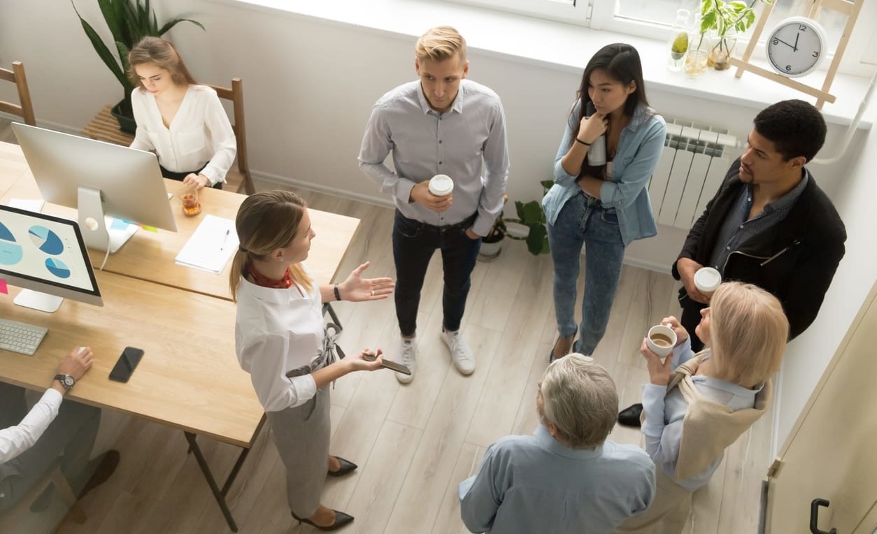 Team leaders meet multiracial interns in office explaining new job, company executives talking to diverse workers listening instructions at break, discussion and computer work in coworking, top view