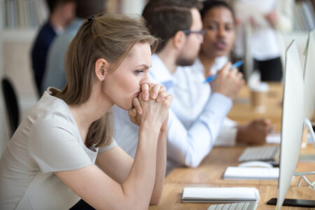 Upset frustrated and confused female worker folding hands on chin feels puzzled having problem troubles and doubts about business moments, sitting in shared modern office with multinational coworkers