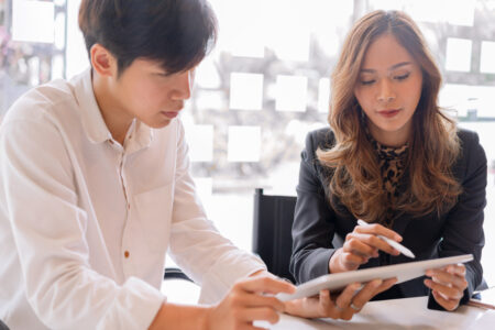 Startup young asian caucasian colleagues discussing work together on tablet, male worker talking to female coworker collaboration concept