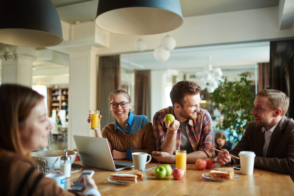 Small team of employees sat at lunch table eating and drinking healthy