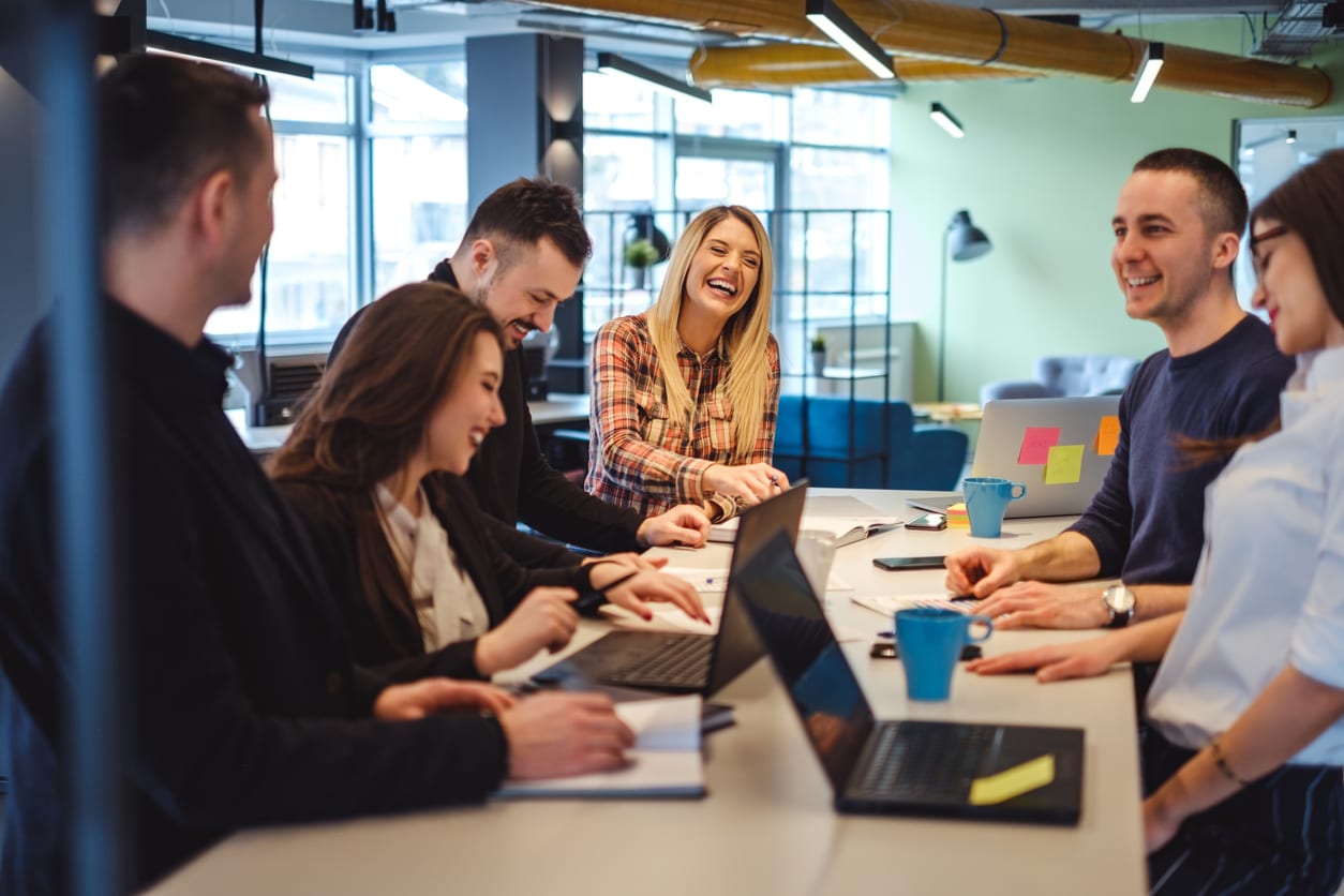 Happy colleagues laughing in the office at the meeting table