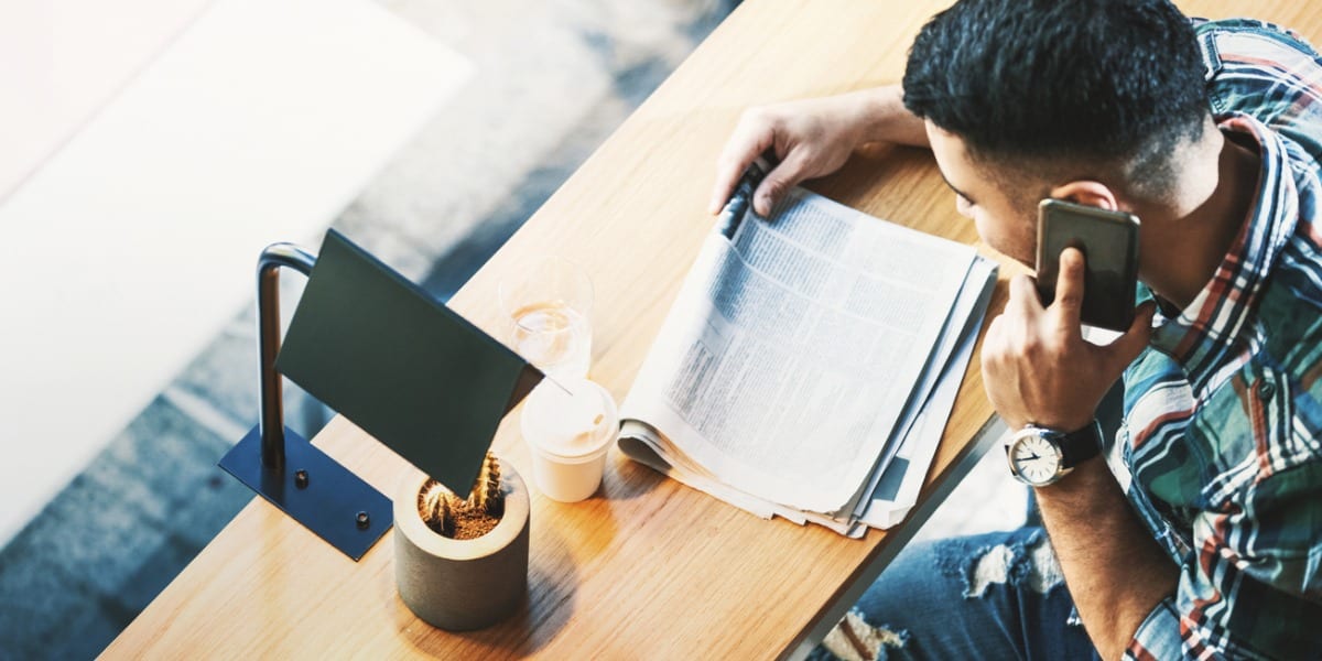 Man reading newspaper on phone and drinking coffee