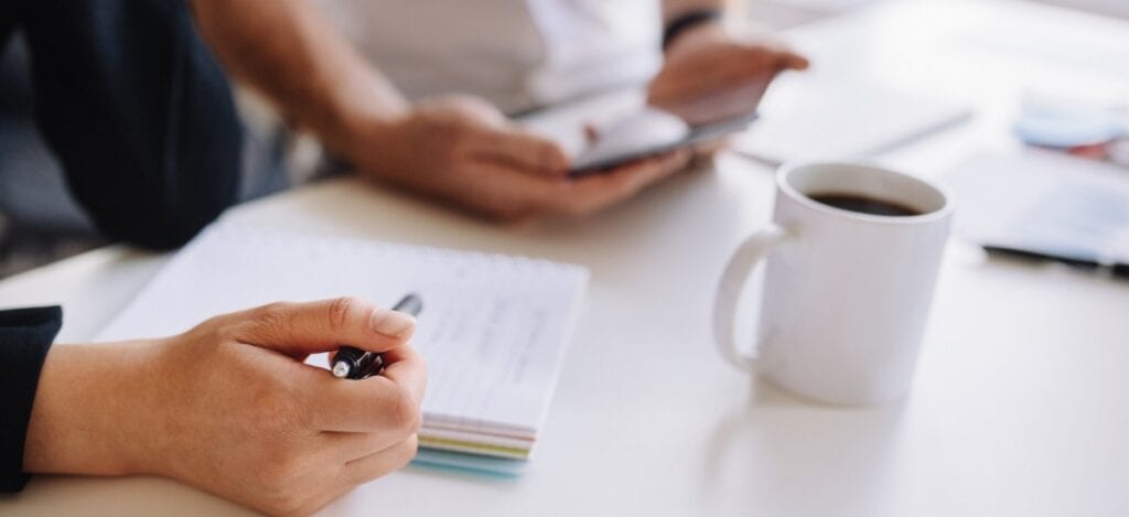 Cropped photo of employees looking at a phone and a notepad