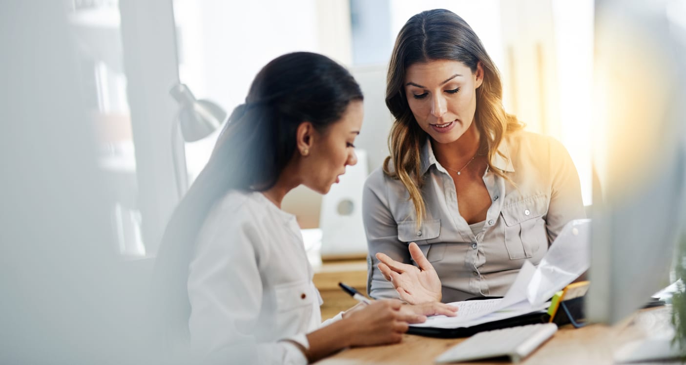 Shot of two young businesswomen talking to each other while being seated in the office at work