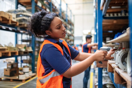 Warehouse worker checking cargo on shelves with scanner. Female worker in uniform scanning boxes in shelves.