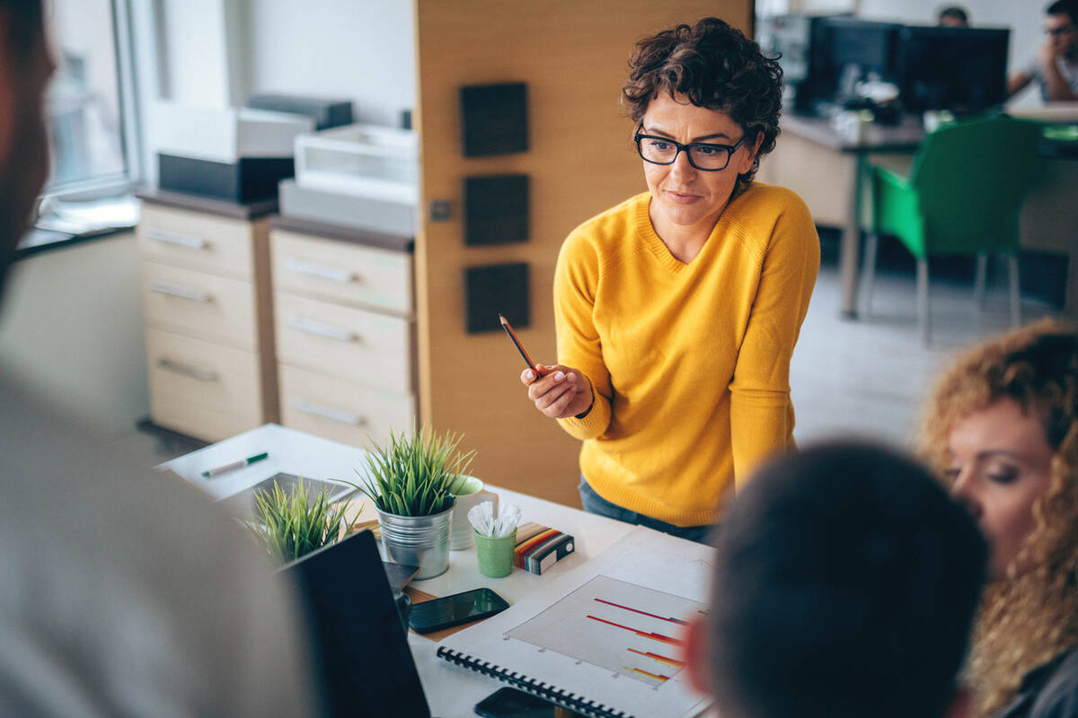 Women in yellow jumper holds pencil whilst in a meeting.