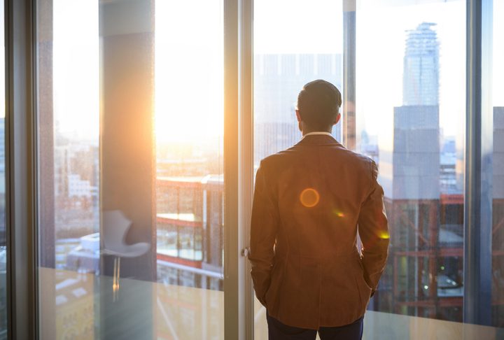 Businessman looking through office window in sunlight