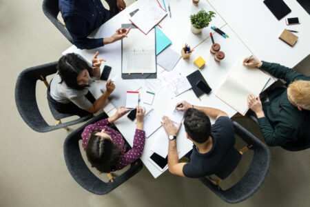 Top view shot of business colleagues discussing over a new project in office. Group of young men and woman brainstorming around table while working on new project.