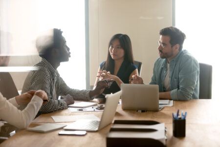 Multiethnic millennial colleagues talk dispute share thoughts on startup project launch at team meeting in office, diverse coworkers brainstorm speak discuss business ideas at briefing together