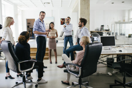 A group of colleagues in a circle are holding a meeting together in a bright, modern office space.