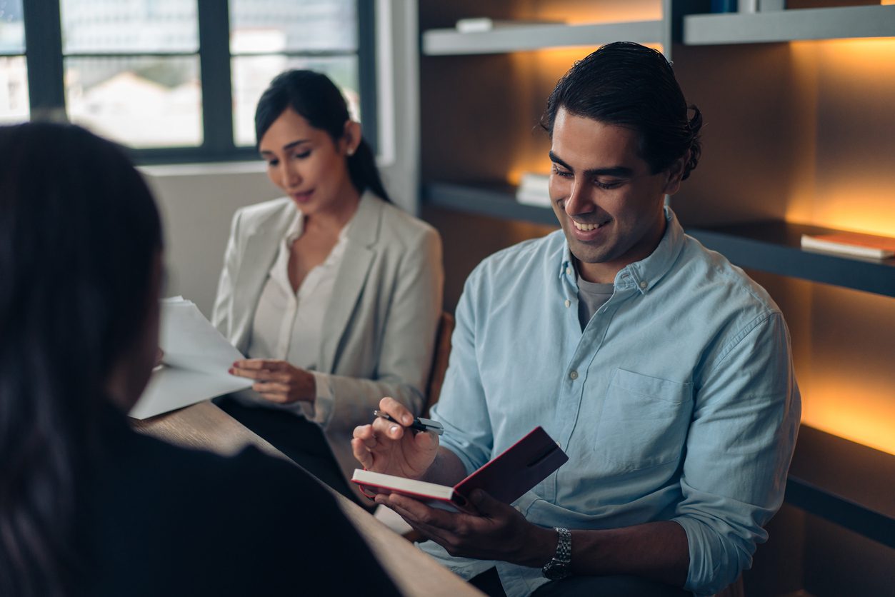 Man smiling at a notepad whilst talking to two employees