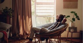 Man with bun in his hair relaxing on a comfy chair in his living room.