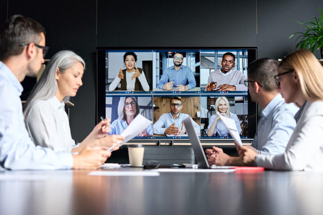 Employees in an office for a meeting on a call with other employees on the big screen