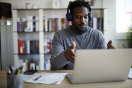 Man with bluetooth headphones having video call on laptop computer in his home office