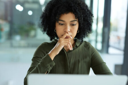 Shot of a young businesswoman looking uncertain while using a laptop in a modern office