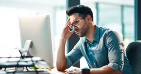 Shot of a young businessman looking displeased while using a computer at his work desk