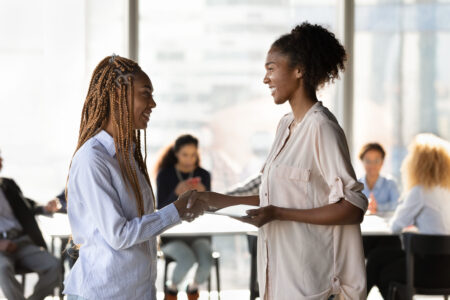 Happy young african american leader shaking hands with biracial colleague, praising for good job or promoting at position in modern office room. Smiling multiracial manager welcoming new worker.