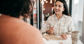 Two women havjng a meeting in a office whilst writing notes