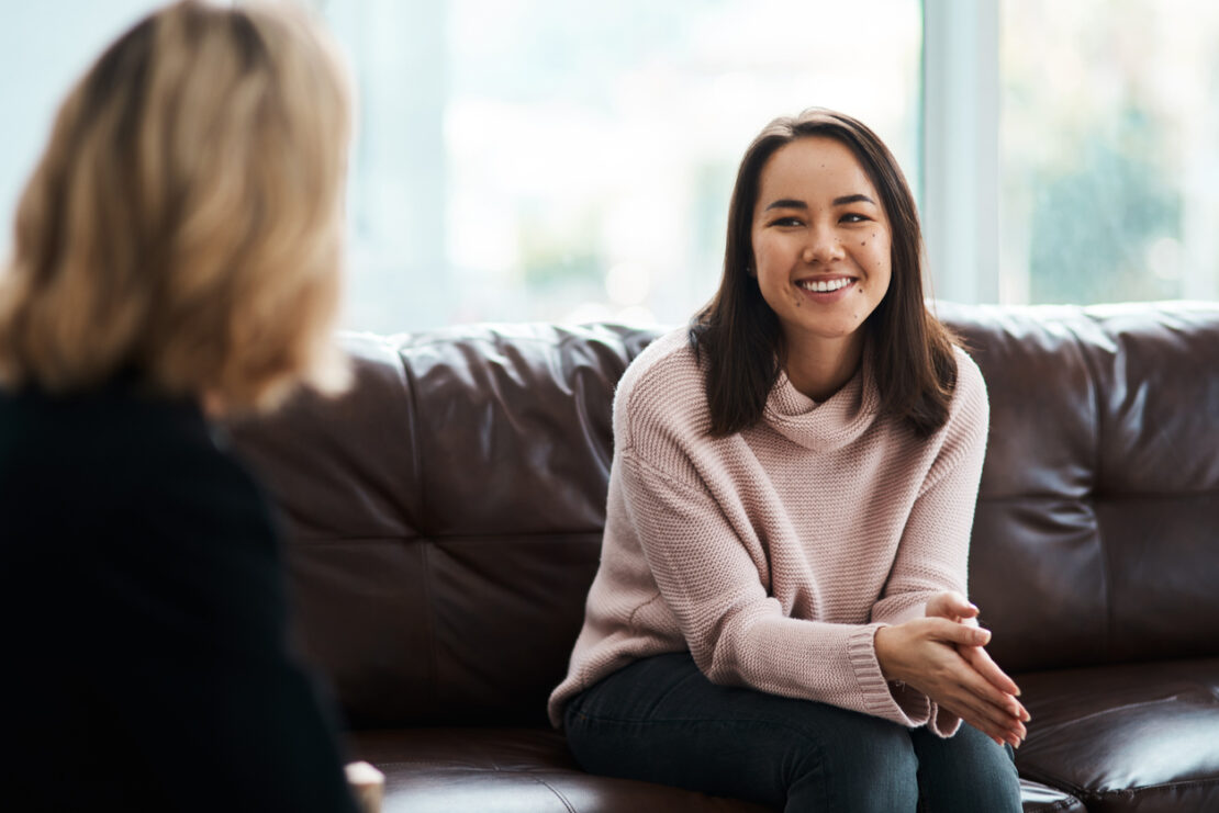 Female sat on couch smiling at another employee.