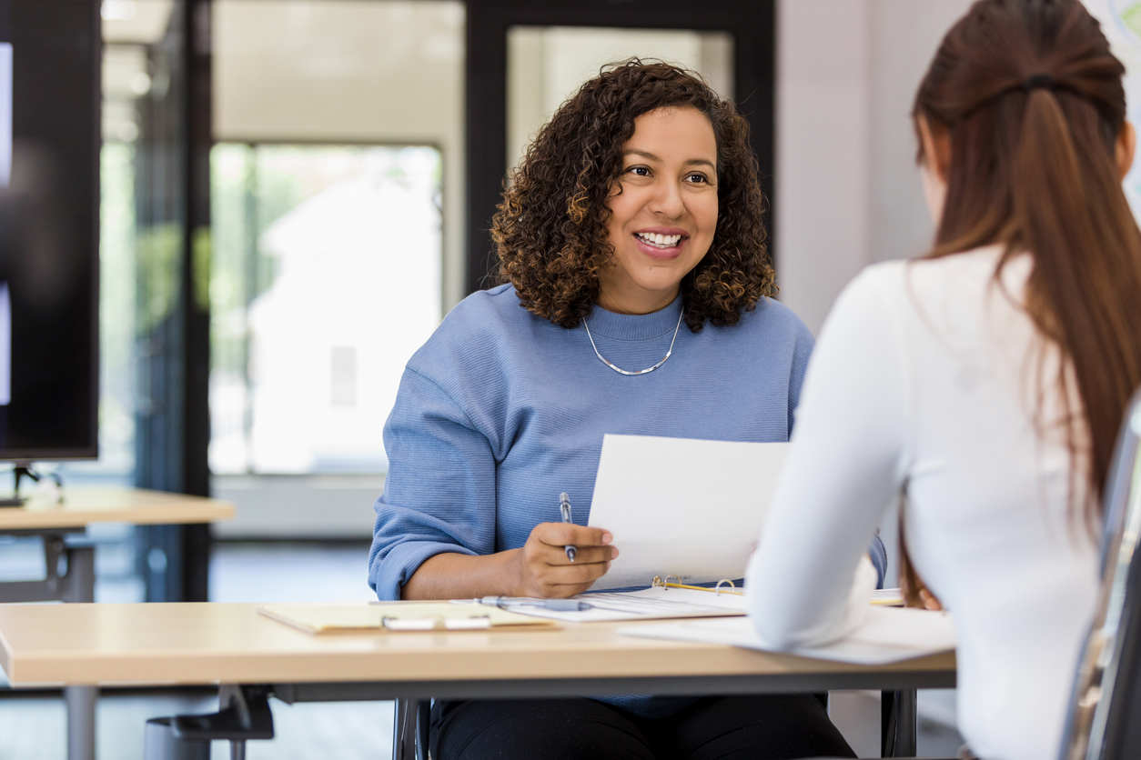 Women in blue jumper interviewing women in a white shirt whilst holding a pen and paper