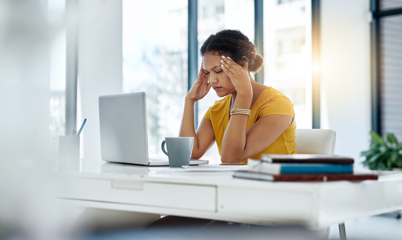 Women in yellow top with hands on her head whilst looking at a laptop