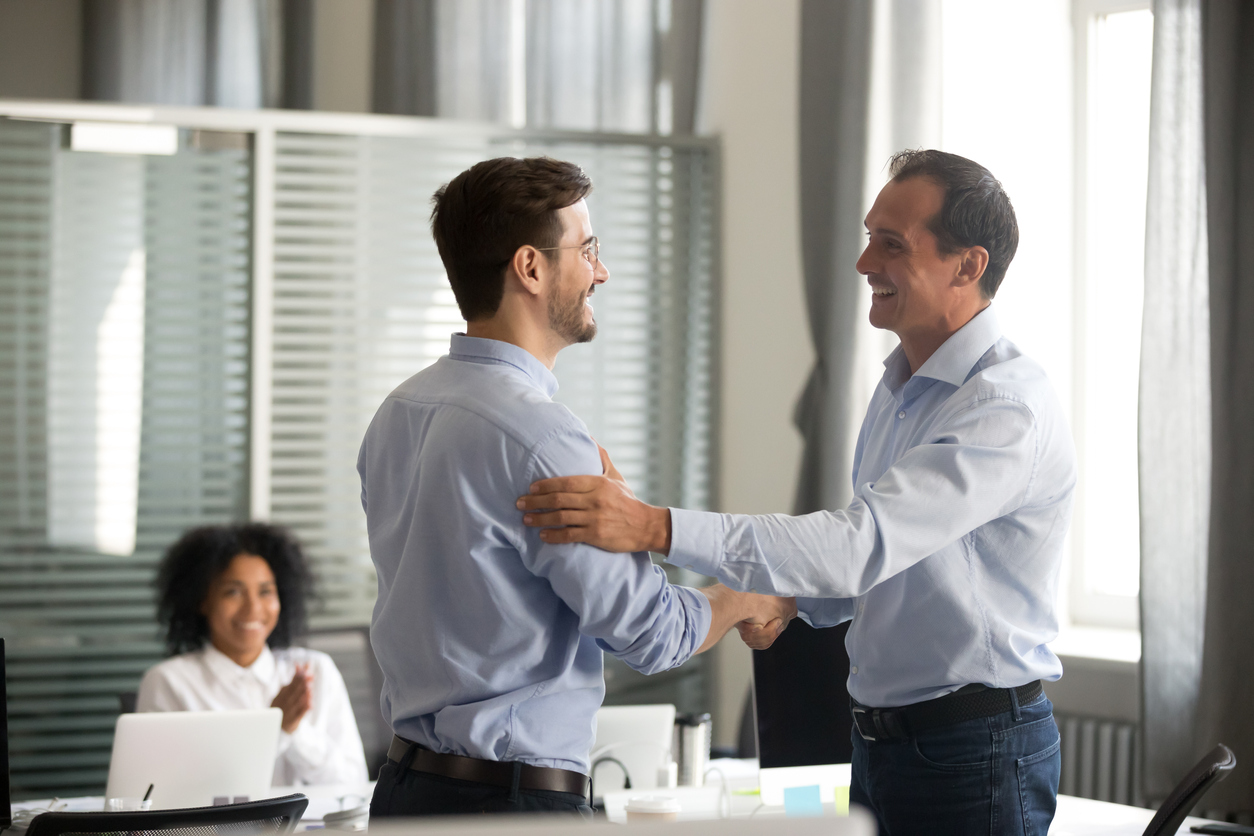 Two male employees shaking hands stood up in smart blue shirts