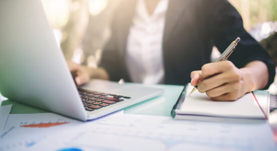 Zoomed in image of womens hands typing on keyboard and writing notes