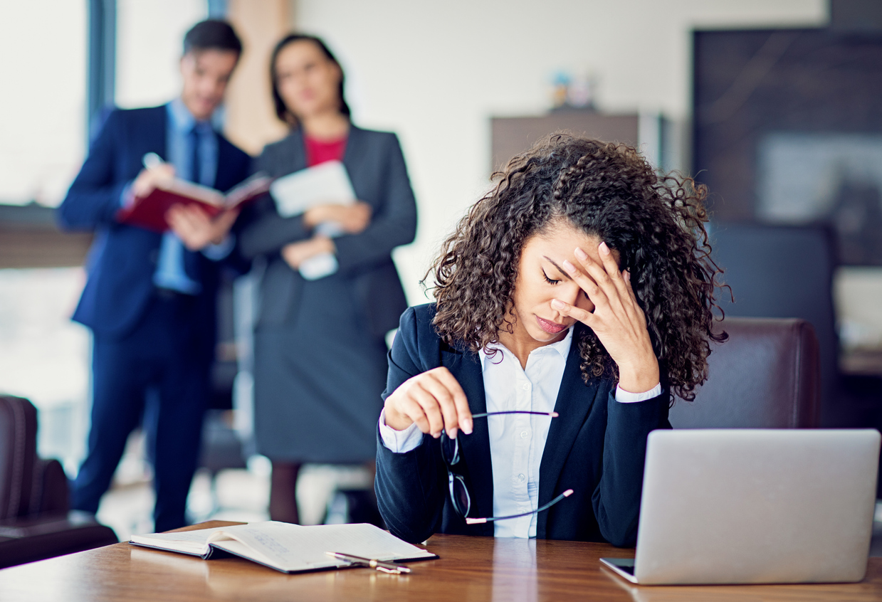 female employee looking stressed at work whilst employees look on