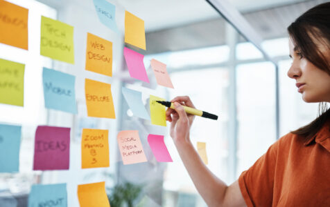 Female employee writing on a sticky note stuck on glass wall