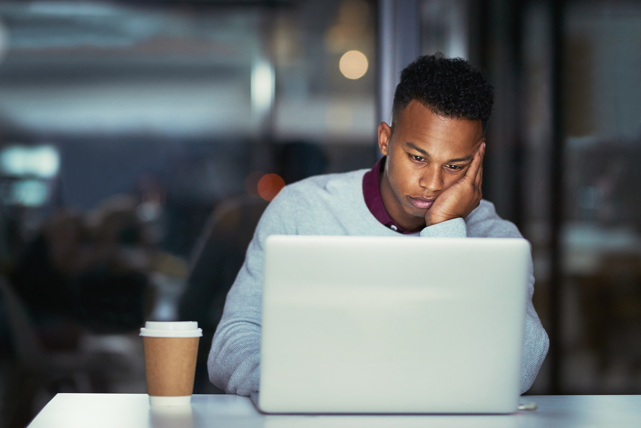 Dark skinned male looking bored at a laptop screen