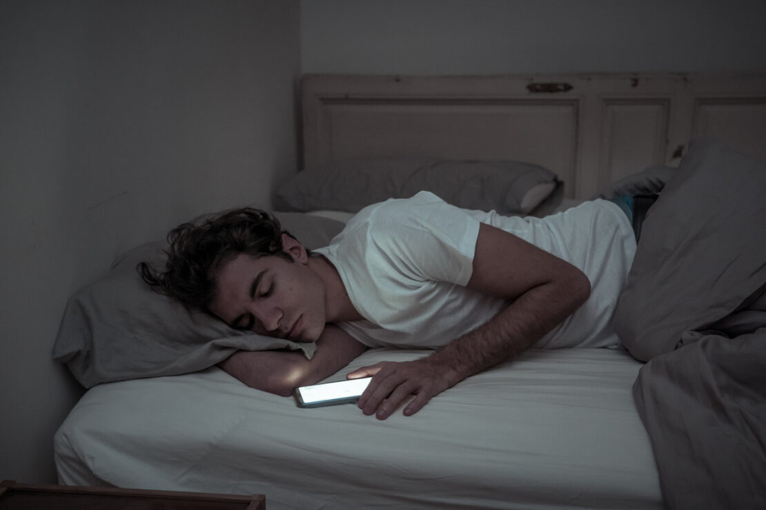 Male asleep in bed with hand still on active phone