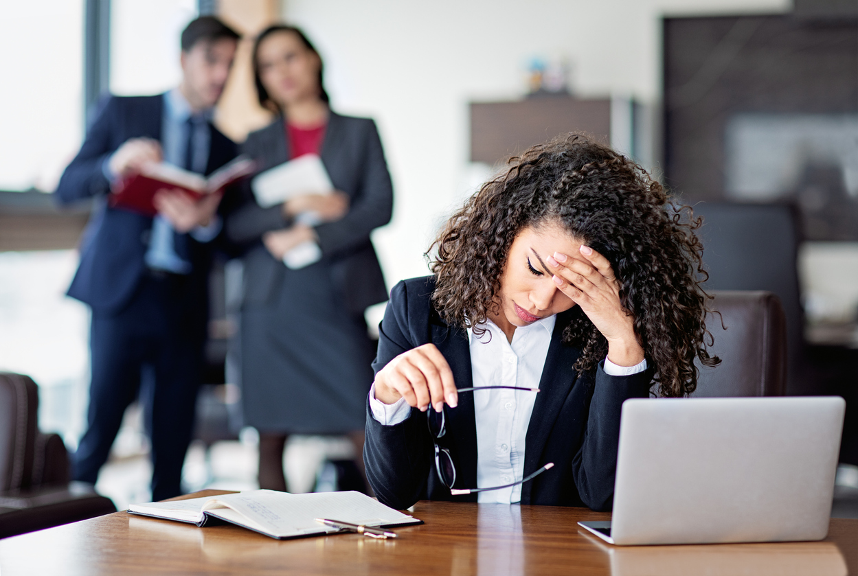 Women with hands on her head stressed whilst coworkers look at her in the background