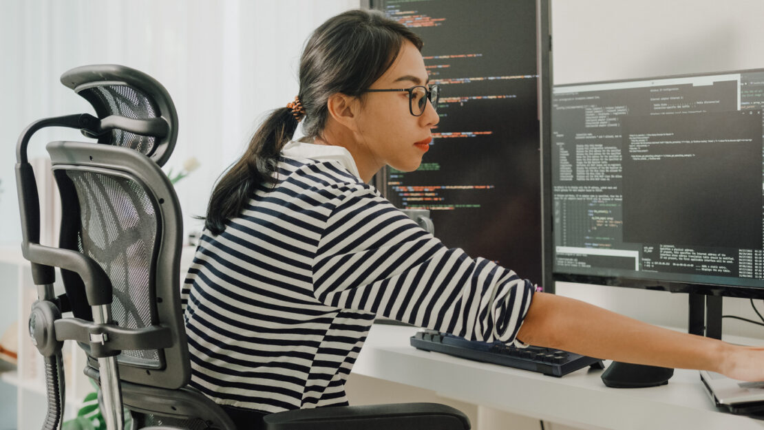 Female software engineer coding on two screens 