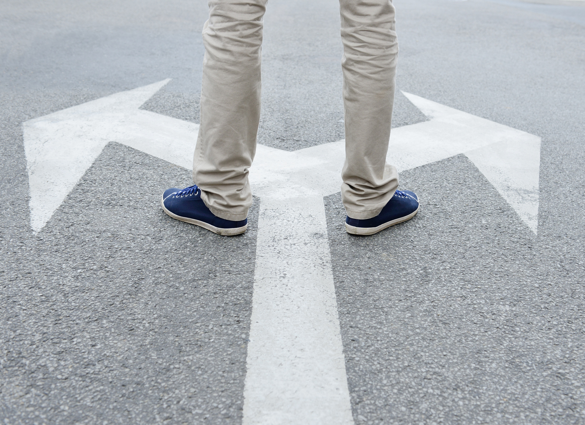 Cropped image of a males feet stood on a arrow pointing two ways