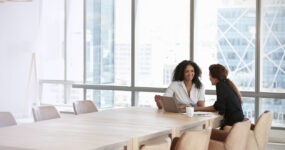 Zoomed out image of two females speaking in a large empty meeting room