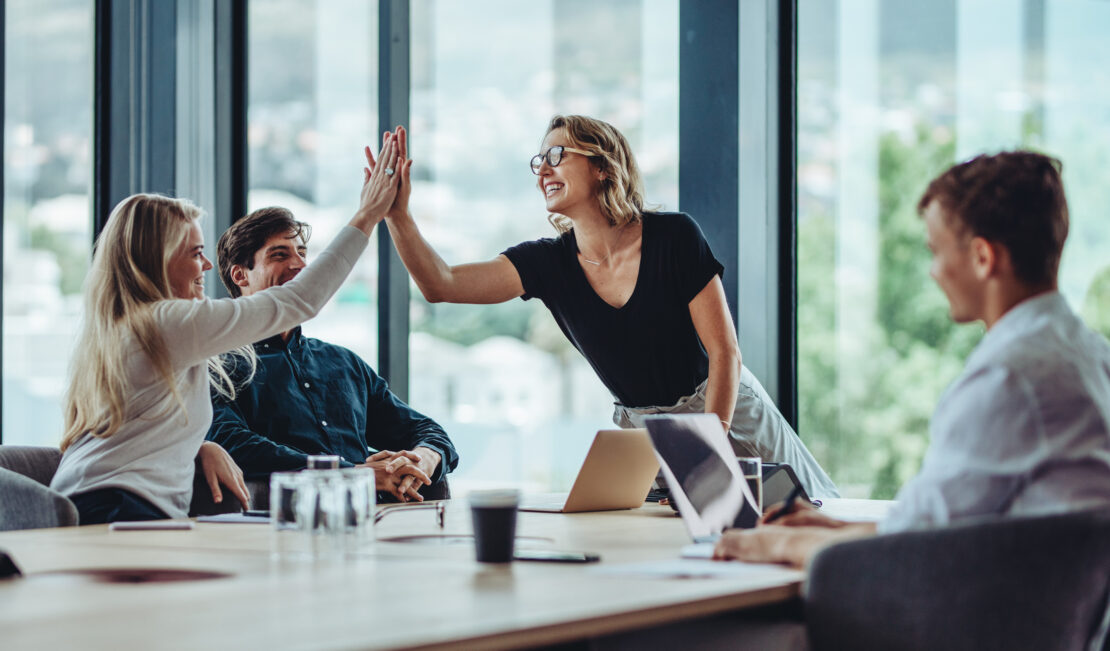 Two male employees watching and smiling at two female employees high fiving