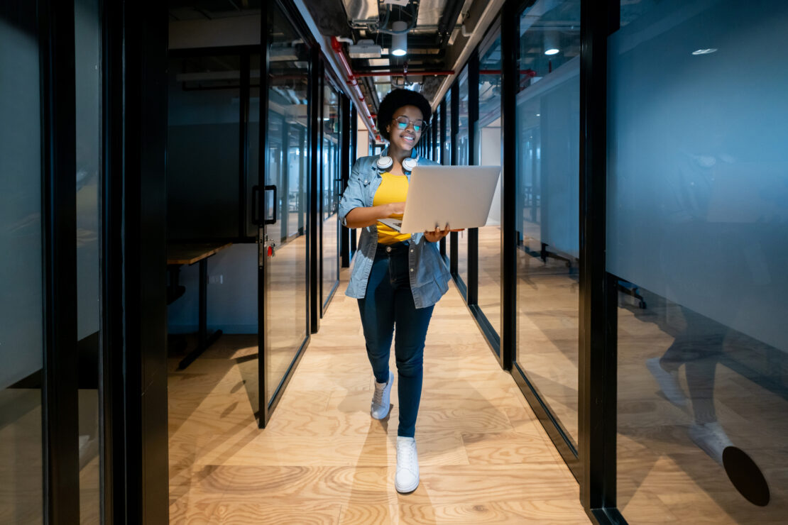 Female walking down office hallway on her laptop smiling