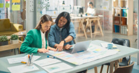 Two females sat together working on printed out paper reports