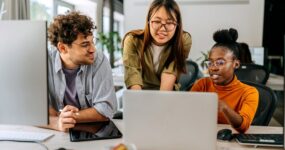 Three employees gathered around laptop speaking about work