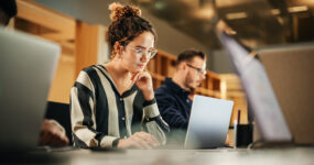 Female employee focused in on her laptop with other employees in the background